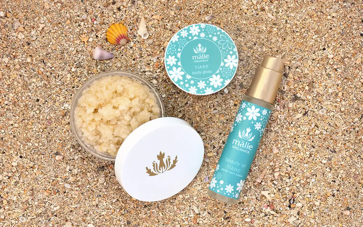 Beauty or skincare products with turquoise and white packaging arranged on sand with seashells.