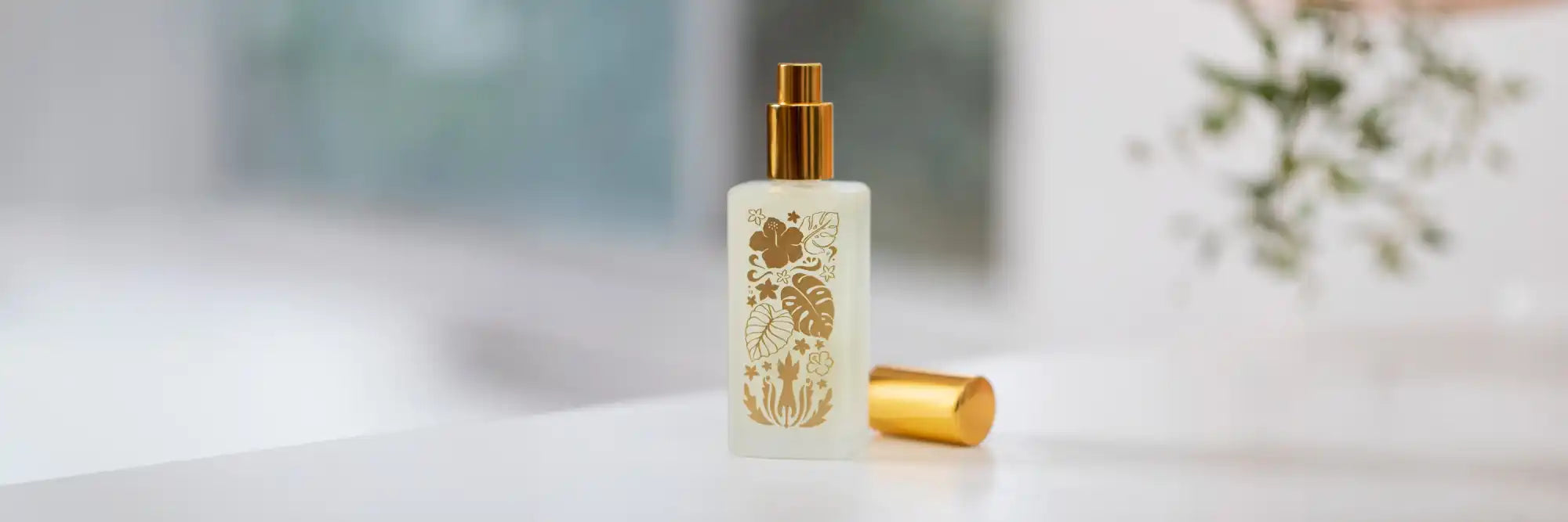 Clear glass bottle with gold cap containing beauty or skincare product featuring floral design elements.