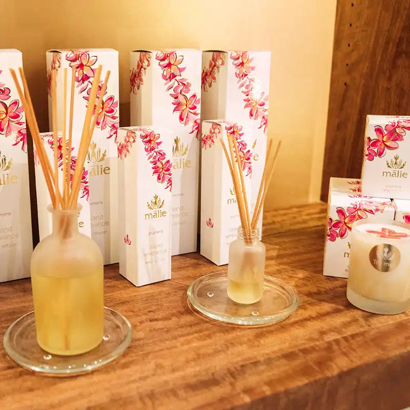 Reed diffusers with floral-patterned packaging boxes displayed on glass coasters.