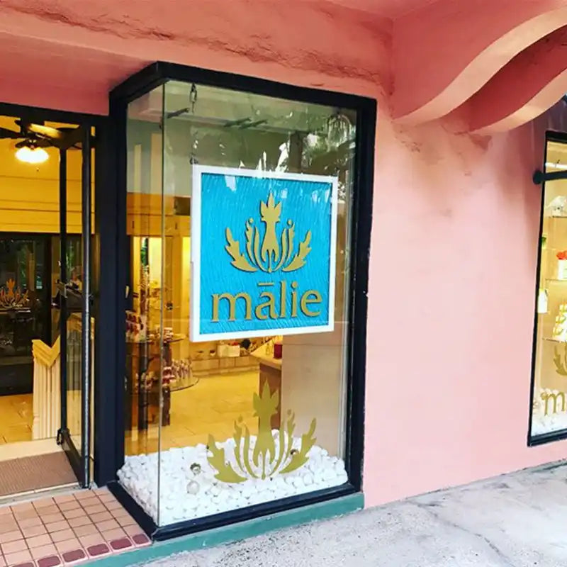 Store sign with ’Malie’ text in blue and gold against a glass display window.