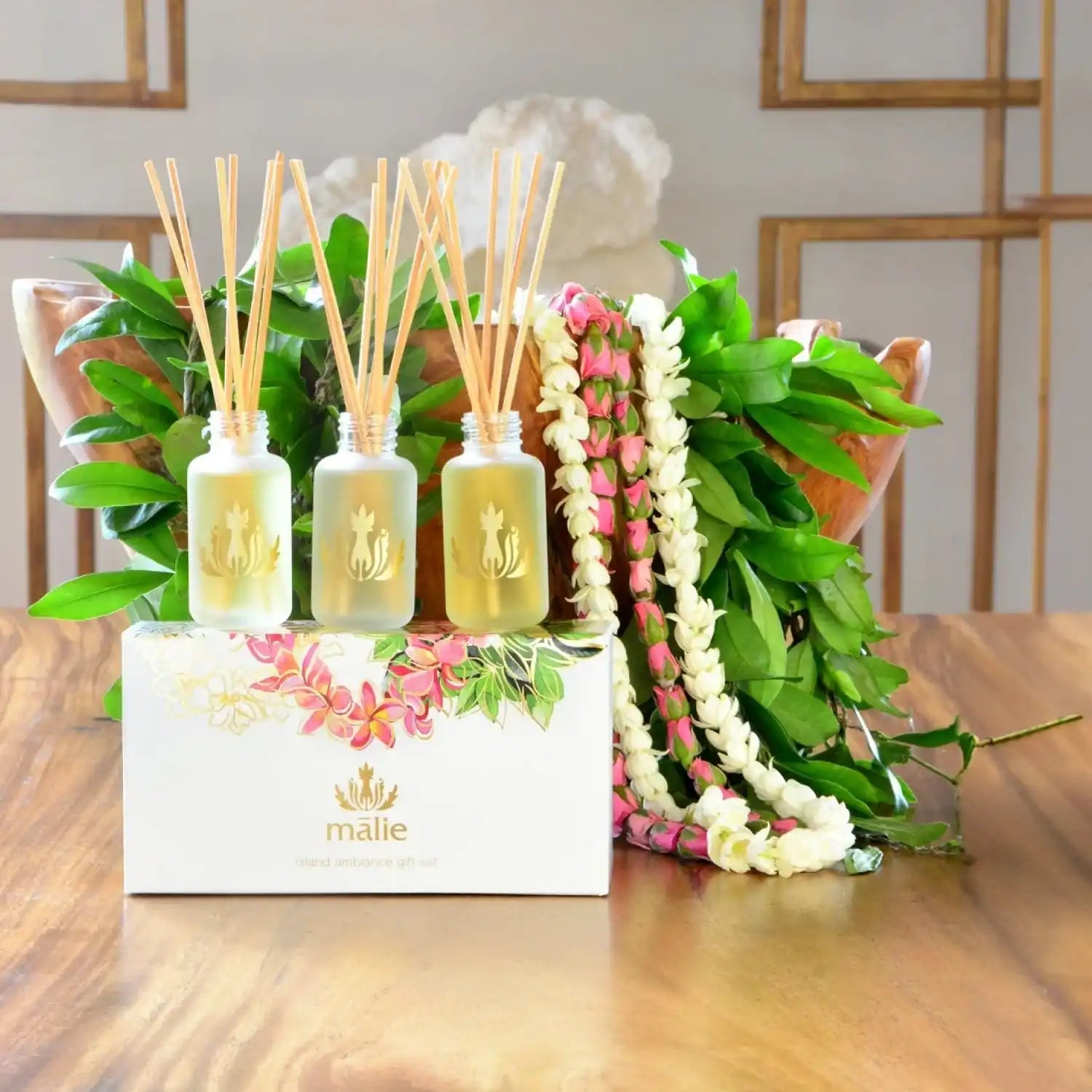 Three reed diffusers with bamboo sticks displayed alongside floral leis.