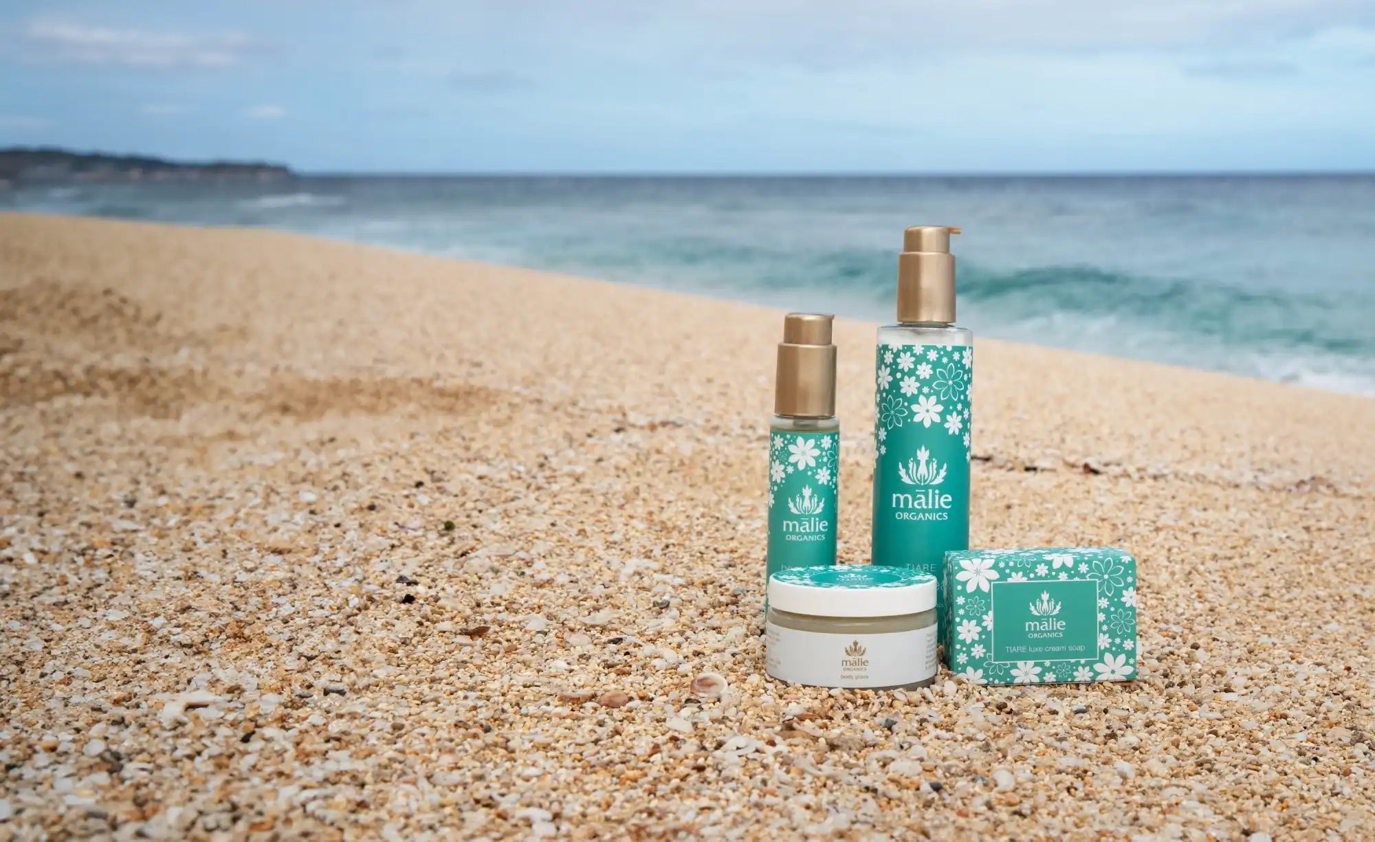 Turquoise beauty or skincare products arranged on beach sand.