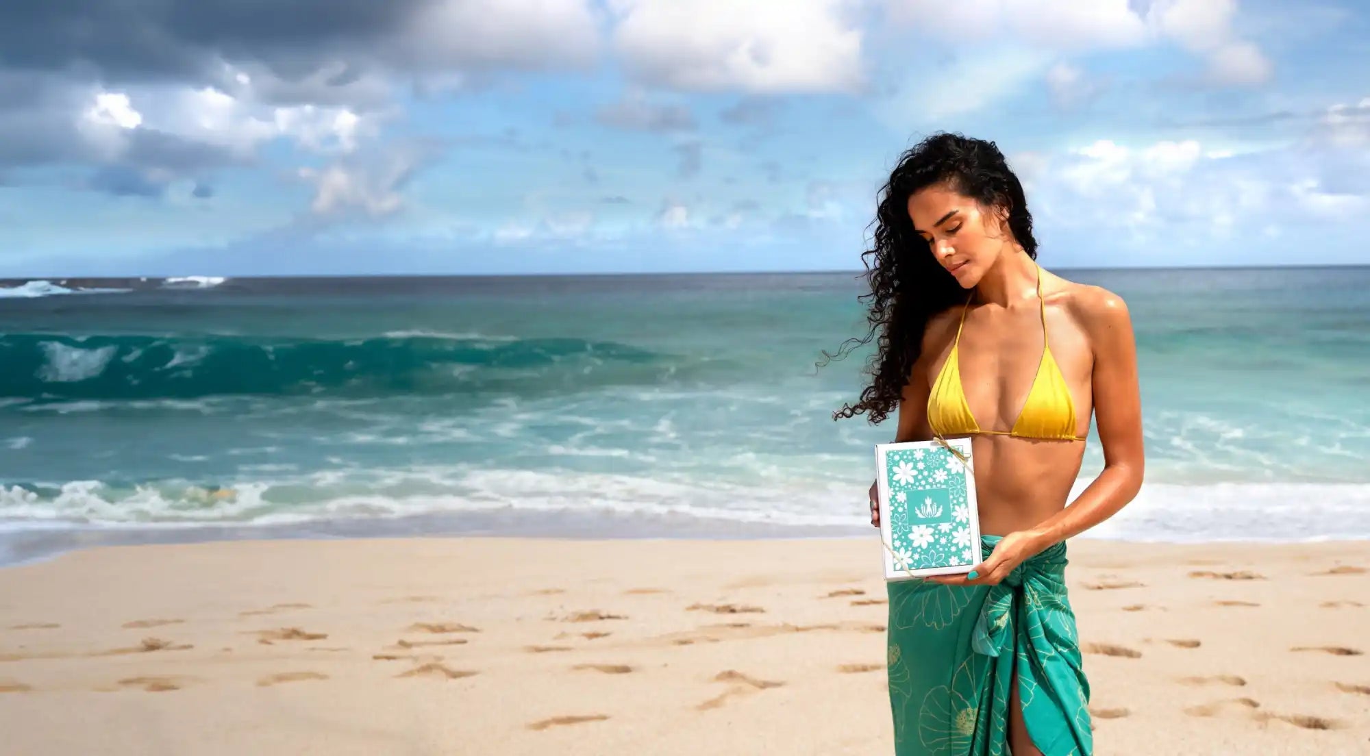 Yellow bikini top with a teal sarong wrap on a beach.